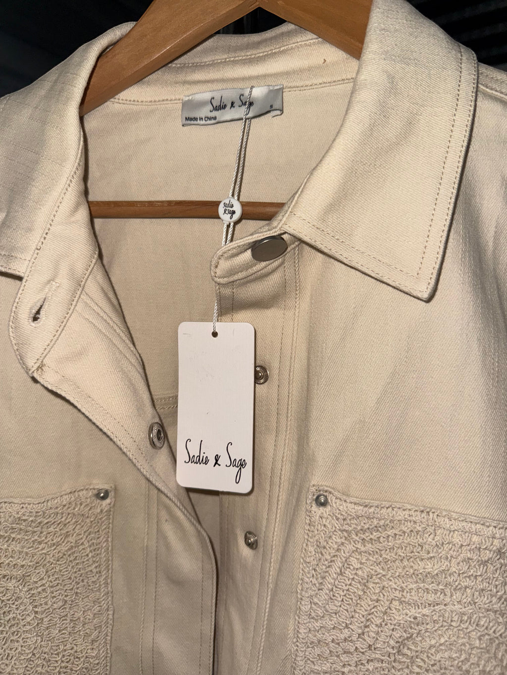 Yanet Collection Shop beige denim jacket with textured pocket detail and silver button closures on a wooden hanger