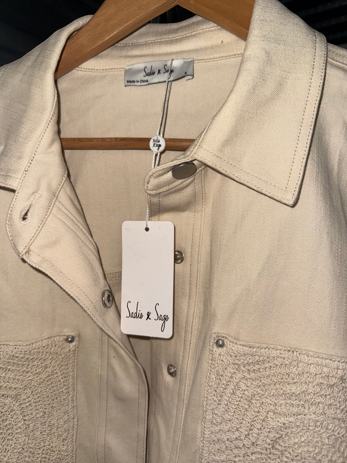 Yanet Collection Shop beige denim jacket with textured pocket detail and silver button closures on a wooden hanger