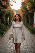 Yanet Collection Shop beige mini dress with square neck and puff sleeves worn by a woman on a cobblestone path