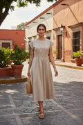 Yanet Collection Shop beige short sleeve maxi dress with a smocked waist, worn by a model on a cobblestone street.