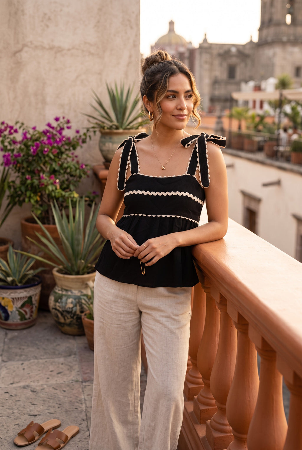 Yanet Collection Shop black spaghetti strap top with ruffled trim and tie shoulders worn by a woman on a balcony