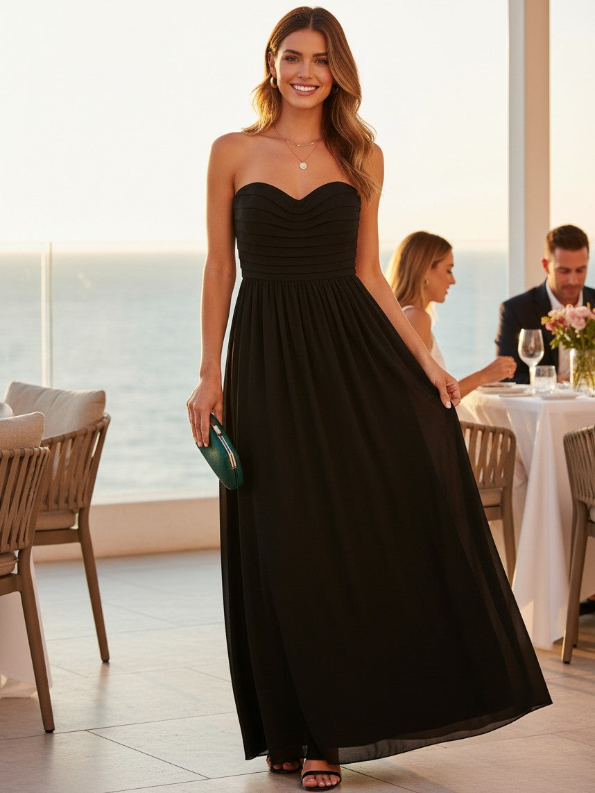 Yanet Collection Shop black strapless maxi dress with a ruffled bodice worn by a smiling woman at an outdoor dinner.
