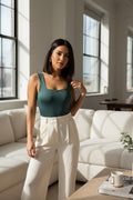 Yanet Collection Shop green sleeveless bodysuit with scoop neckline worn by a woman with white trousers in a bright room
