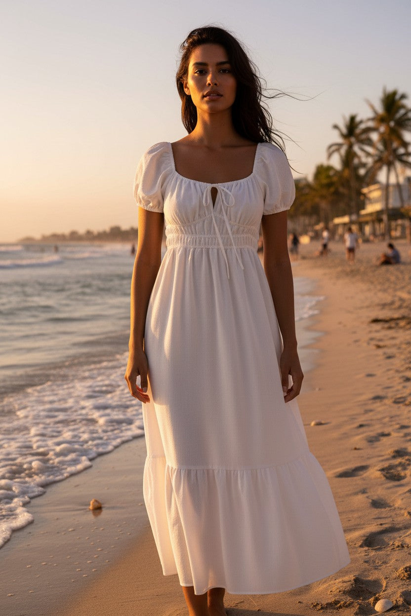 Yanet Collection Shop ivory maxi dress with puff sleeves, smocked bodice, and ruffled hem worn by a model on a beach