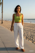 A woman wearing a Yanet Collection Shop lime green sleeveless textured crop top with white linen trousers on a beach
