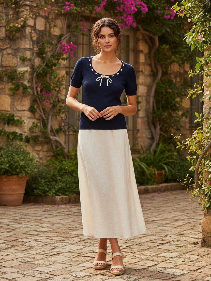 Yanet Collection Shop navy short sleeve top with white decorative tie detail and round neck worn with a cream skirt.