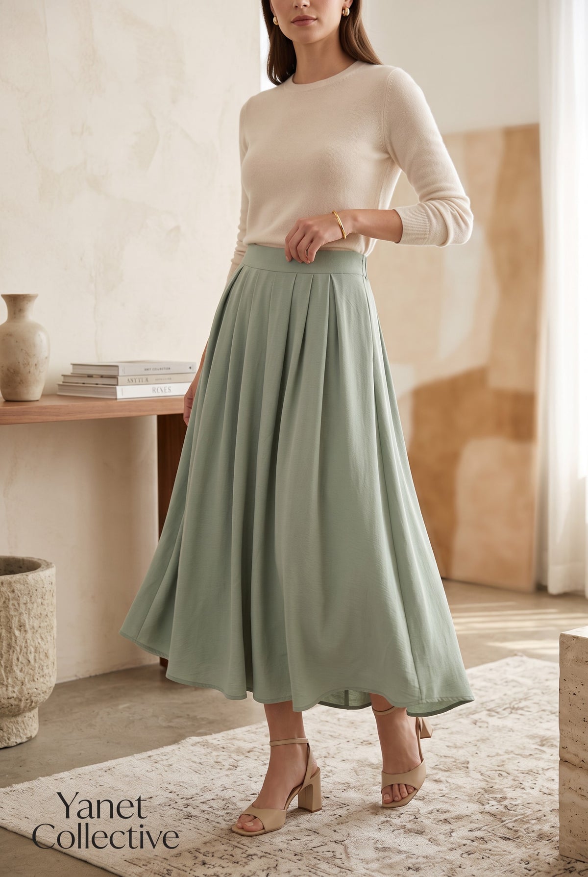 Yanet Collection Shop sage green high-waist pleated maxi skirt worn by a model with a beige sweater and heels.