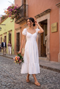 Yanet Collection Shop white smocked maxi dress with puff sleeves and ruffle hem worn by a woman on a cobblestone street